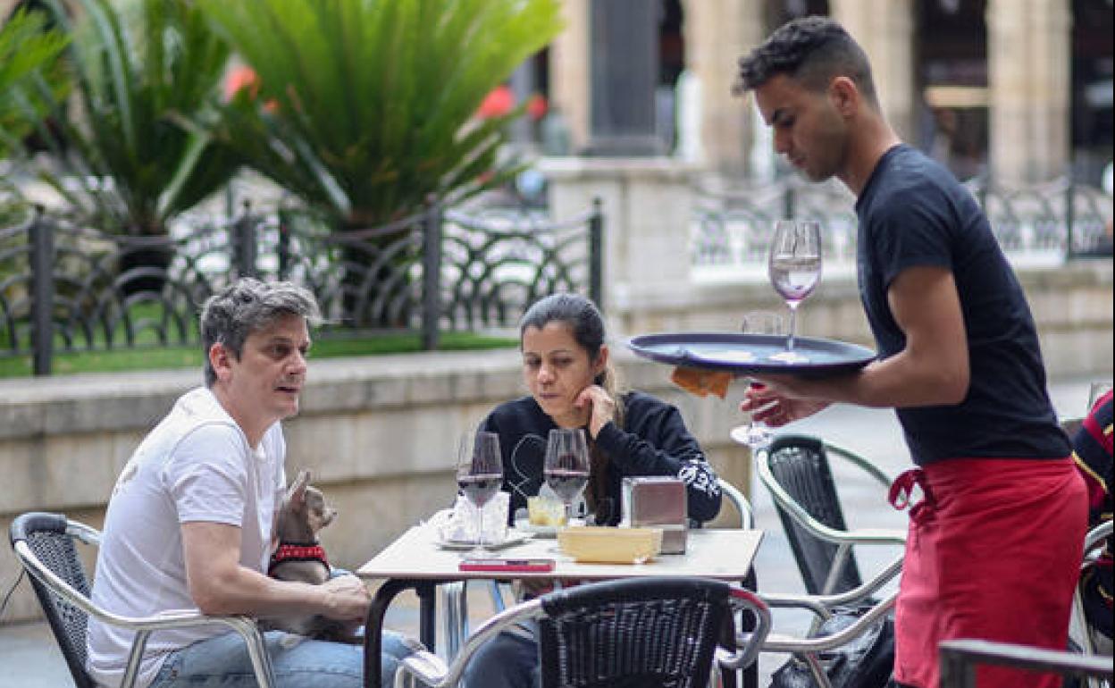 Camarero junto a unos clientes en la terraza de un bar, este verano. 