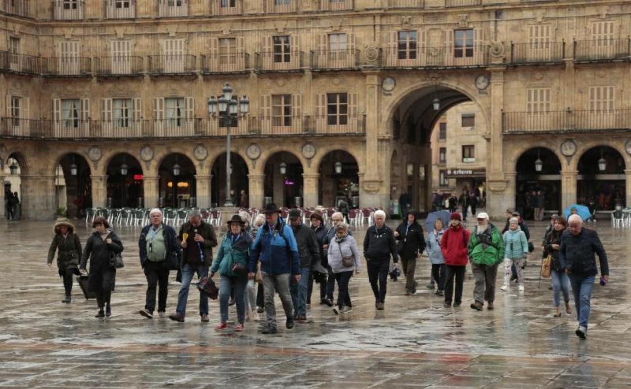 Un grupo de turistas camina bajo la lluvia en la Plaza Mayor.