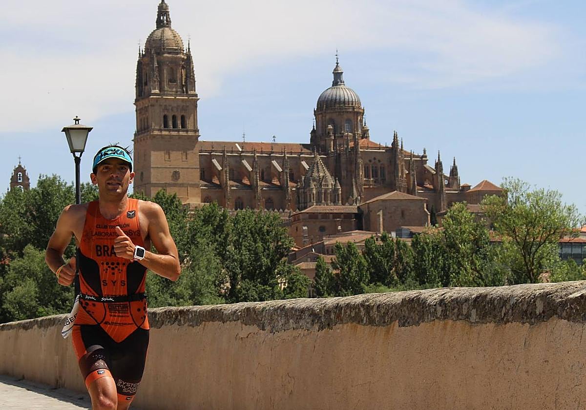El triatleta Alberto Bravo corriendo por el Puente Romano de Salamanca con las catedrales de fondo.