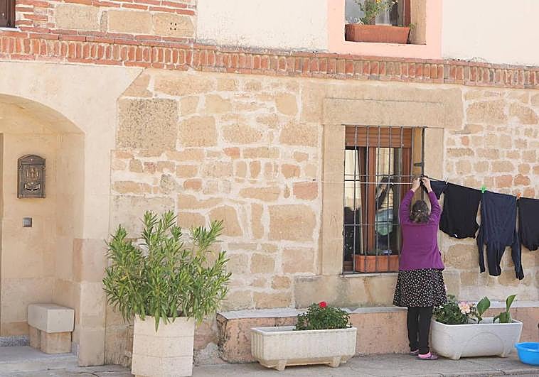 Una mujer tiende la ropa en la fachada de su casa.