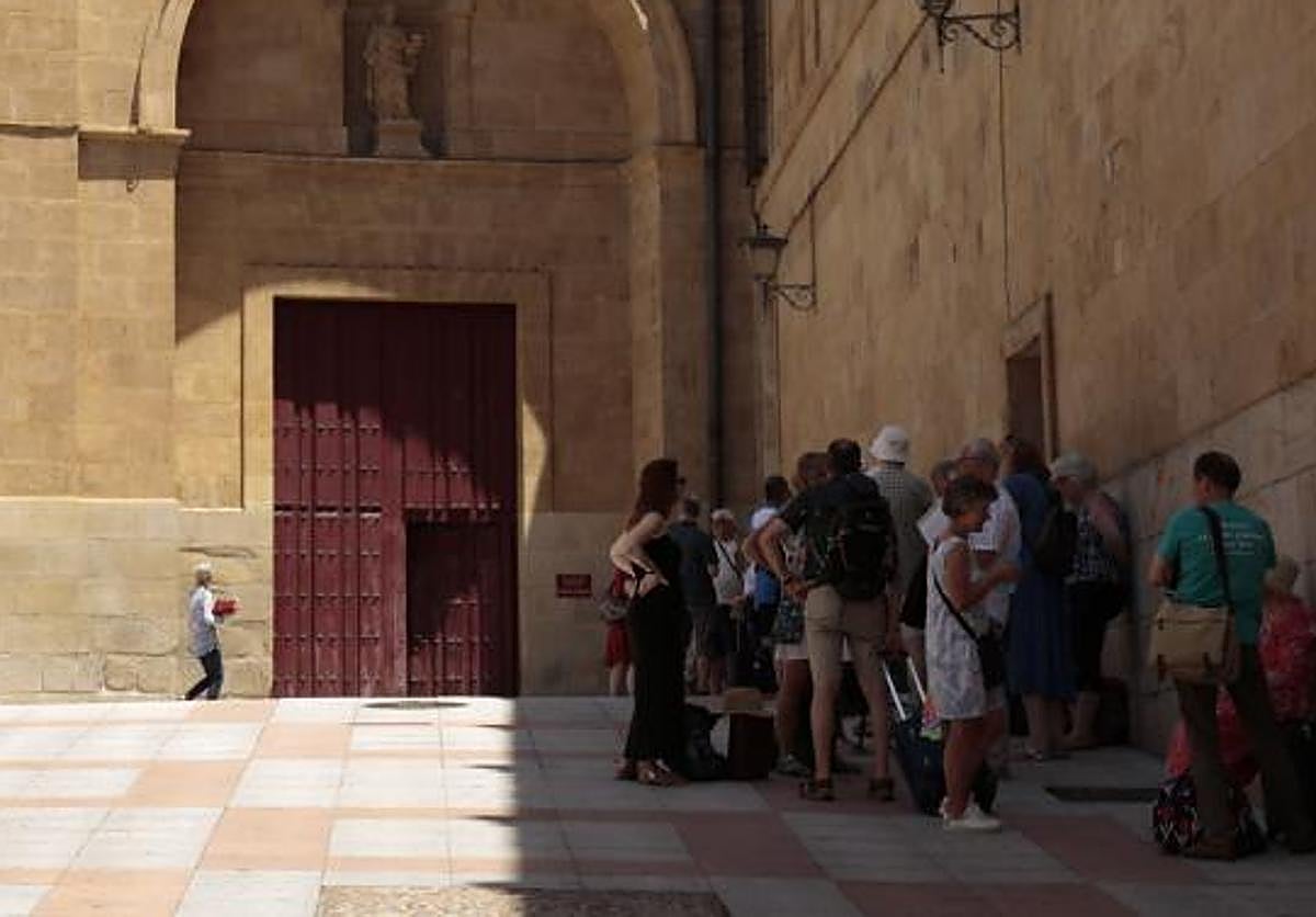 Un grupo de turistas se protege del calor en una sombra junto a la catedral.