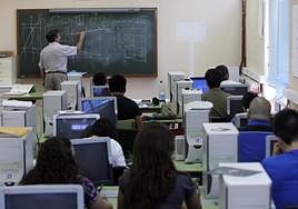 Un profesor escribe en la pizarra en un aula con ordenadores.