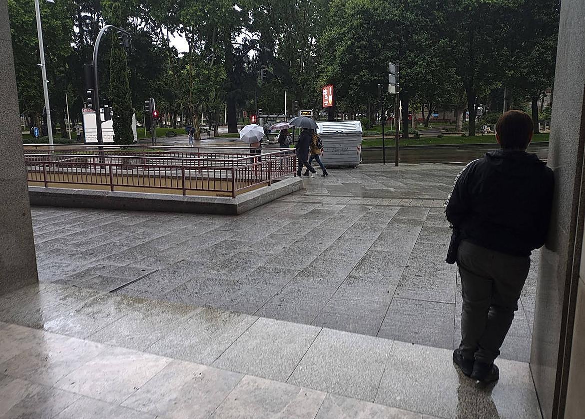 Una mujer aguarda en un portal a que deje de llover.