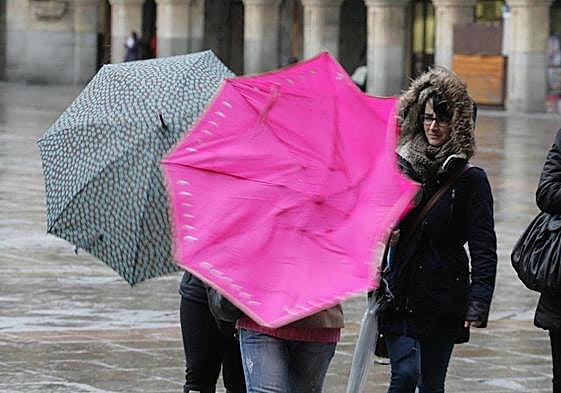Dos personas sujetan un paraguas en la Plaza Mayor.
