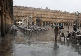 Varias personas pasean bajo la lluvia en la Plaza Mayor de Salamanca.