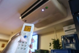 Una persona manipula el mando de un sistema de aire acondicionado.