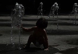Un niño se refresca en una fuente de chorros al anochecer.