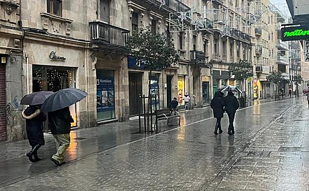 Varias personas pasean con paraguas a las 17:15 horas por la calle Azafranal de Salamanca para protegerse de la lluvia iniciada minutos antes.