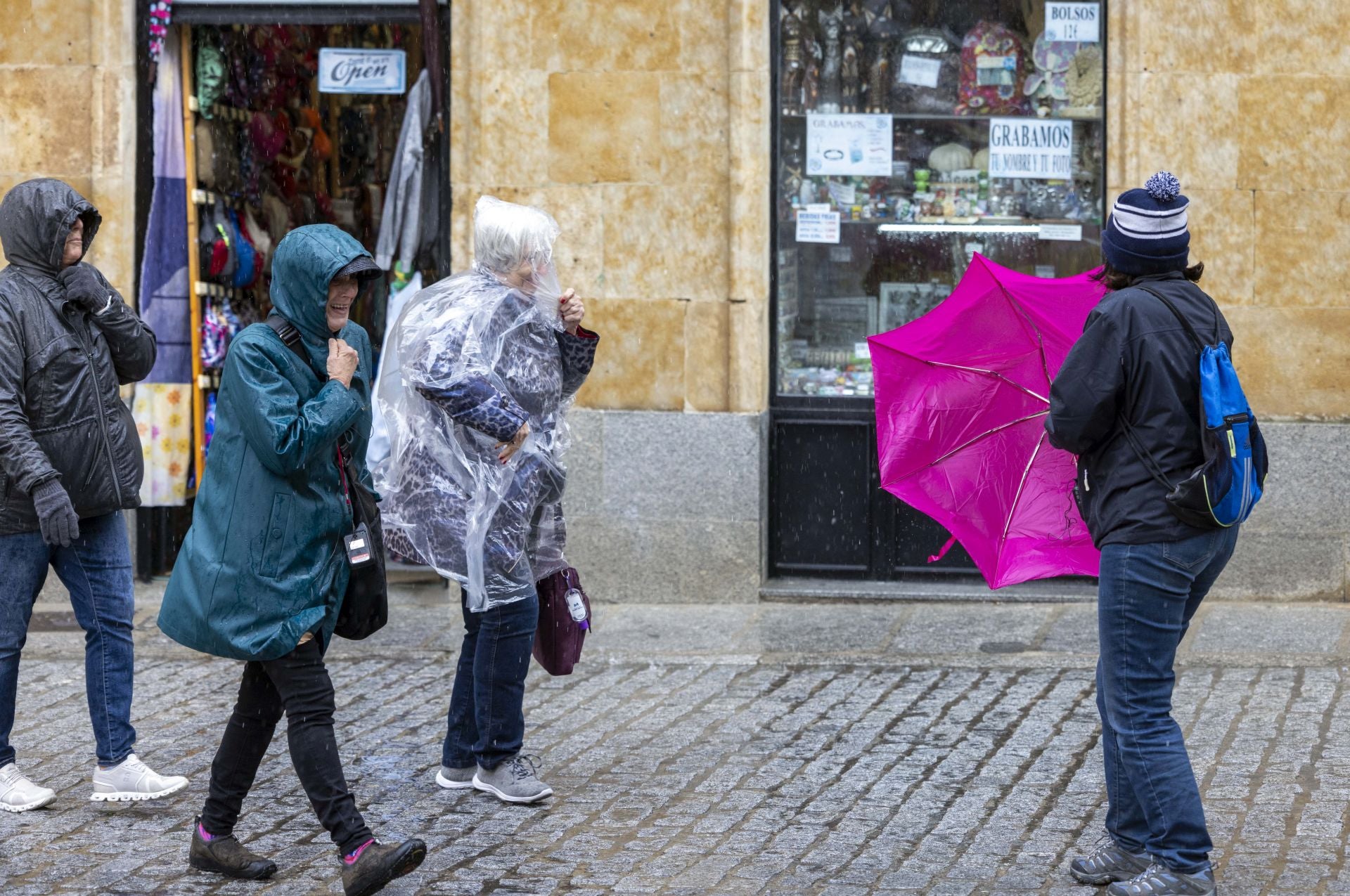 Varias personas pasean con paraguas y chubasqueros por Salamanca.