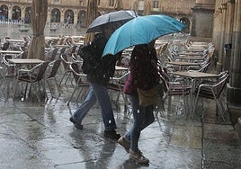 Dos personas pasean por la Plaza Mayor con sus paraguas un día de lluvia.