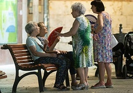 Unas mujeres se abanican sentadas en un banco a la noche.