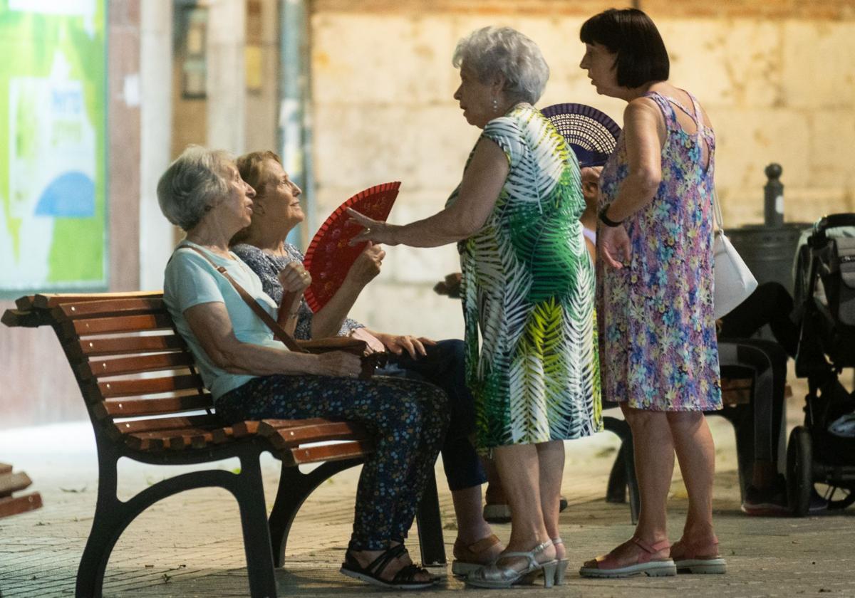 Unas mujeres se abanican sentadas en un banco a la noche.