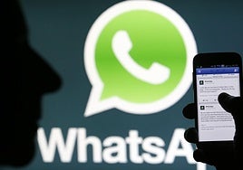 Vista de un teléfono con la aplicación de Facebook , con el logotipo de Whatsapp al fondo.