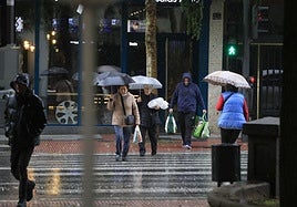 Varias personas pasan un paso de cebra protegidos con un paraguas.