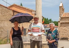 Ángeles und Julia, zwei Einwohnerinnen von Valderrebollo, auf der Plaza Mayor des Dorfes, neben Curro, der einen Lachs hält, wie er ihn ab 2028 vermarkten möchte.