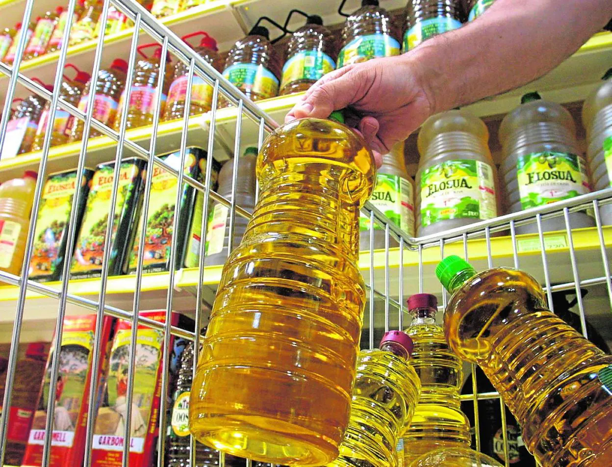 A customer selects several bottles of oil from the shelves of a supermarket. 