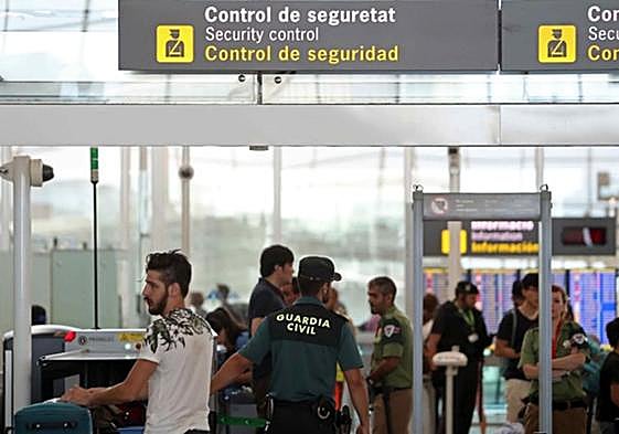 Passengers queue at an airport security control.