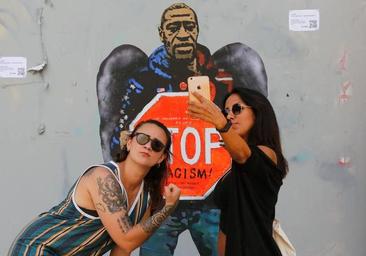 Two women stand next to a mural of George Floyd, who was killed by police in the United States.