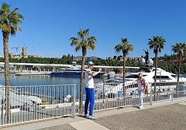 Tourists take photos with the megayachts moored in the port of Malaga.
