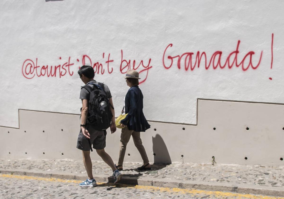 A couple stroll through the Albaicín in front of anti-tourist graffiti in 2019.