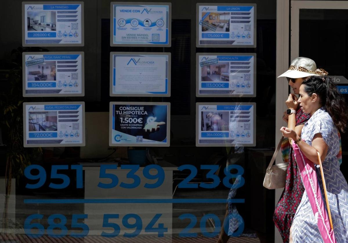 Women stroll past the window of a real estate agency this summer.