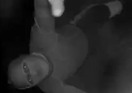 A masked burglar attempts to tamper with a security camera.