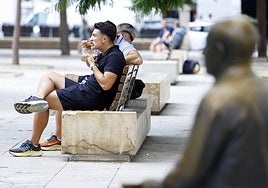 A tourist eats a salad on a bench in the Plaza de la Merced under the 'gaze' of Picasso.