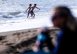 A young couple take the plunge in the sea while others enjoy the beach.