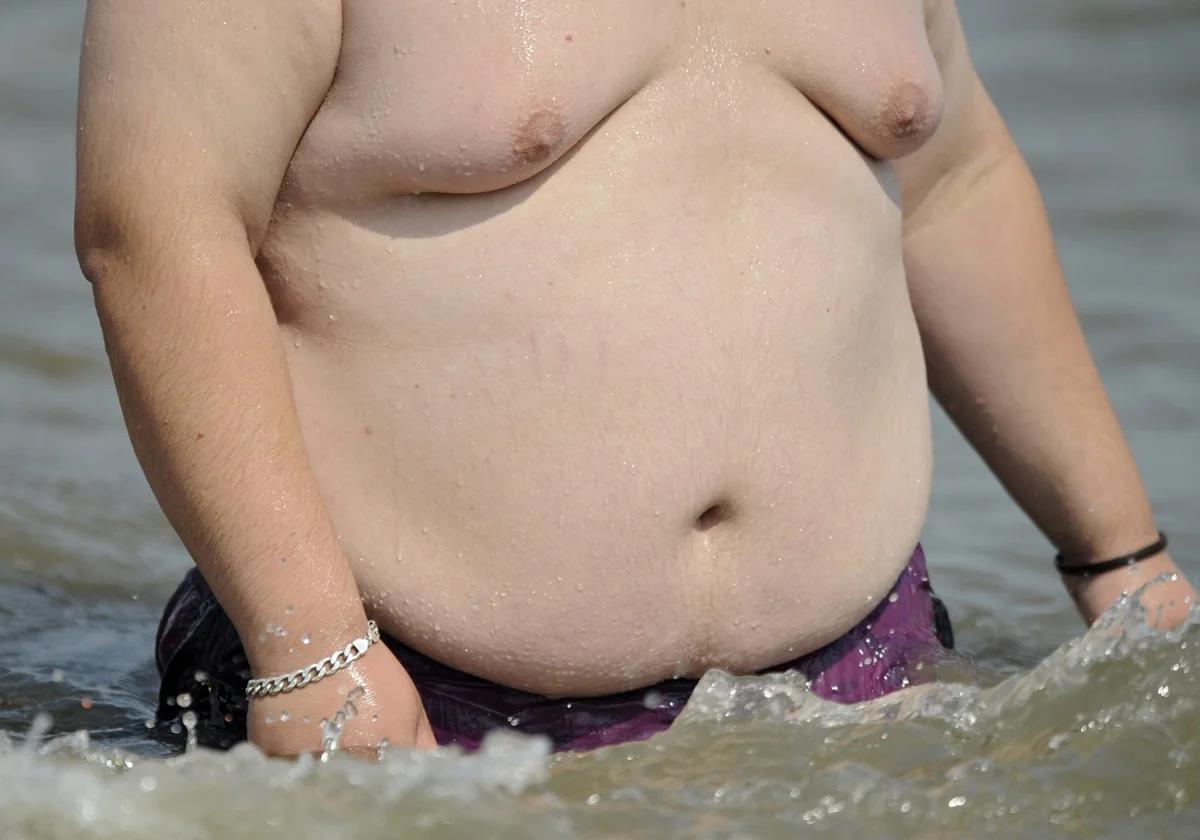 An obese man emerges from the sea on a beach in Spain.