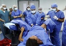 A doctor delivers a baby while a group of medical students look on.