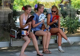 Three tourists dodge the Spanish summer heat by fanning themselves on a park bench in the shade.