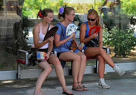 Three tourists dodge the Spanish summer heat by fanning themselves on a park bench in the shade.