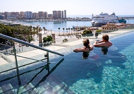 Tourists enjoy a hotel swimming pool overlooking the port in Malaga city.