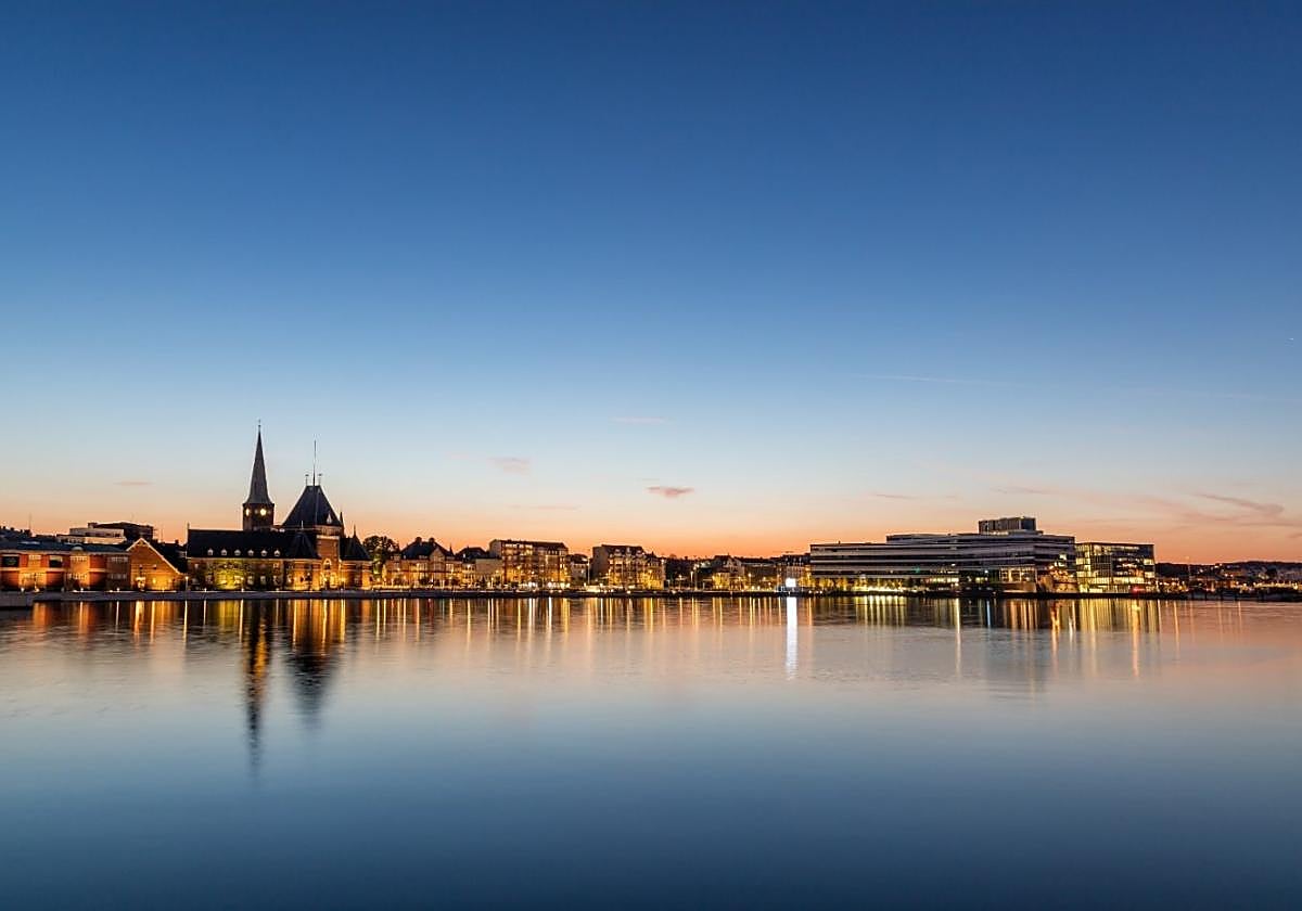 Sun setting over Aarhus' city skyline with the Domkirke spire and port buildings lining the water.