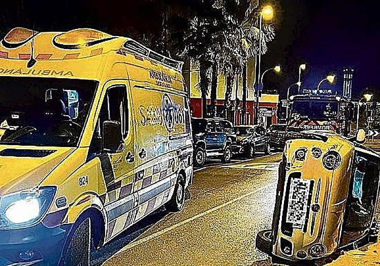 An ambulance comes to the aid of the driver of an overturned car.