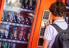 A schoolboy inserting coins into a vending machine that sells energy drinks.