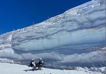 Two skiers in adapted equipment next to the snow wall of the Laguna chairlift, next to the Veleta peak.