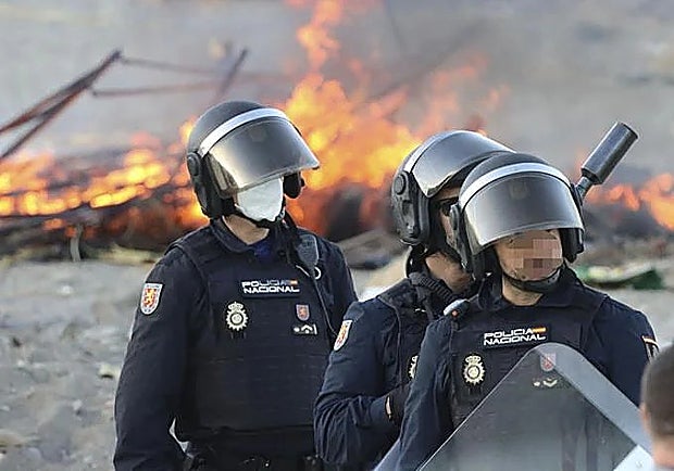 National Police officers standing in front of burning migrants' settlements.
