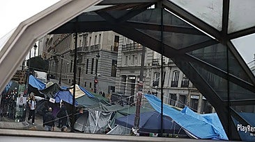 Tents reflected in the glass at the entrance to Sol station in Madrid.