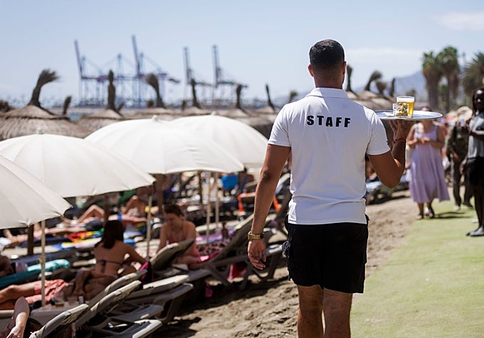 A waiter serving drinks to customers in the sun loungers at a beach bar.