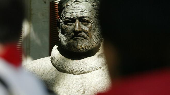 Revellers wearing the traditional San Fermín red scarves walk past the bust of Hemingway in Pamplona. 