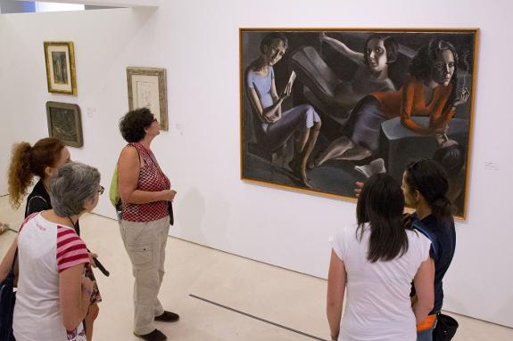 A group of women looking at 'Tertulia' (1929) by Spanish artist Ángeles Santos (1911-2013), on loan from the Reina Sofía Art Museum, which is one of the 124 works in the temporary exhibition at the Picasso Museum in Malaga.