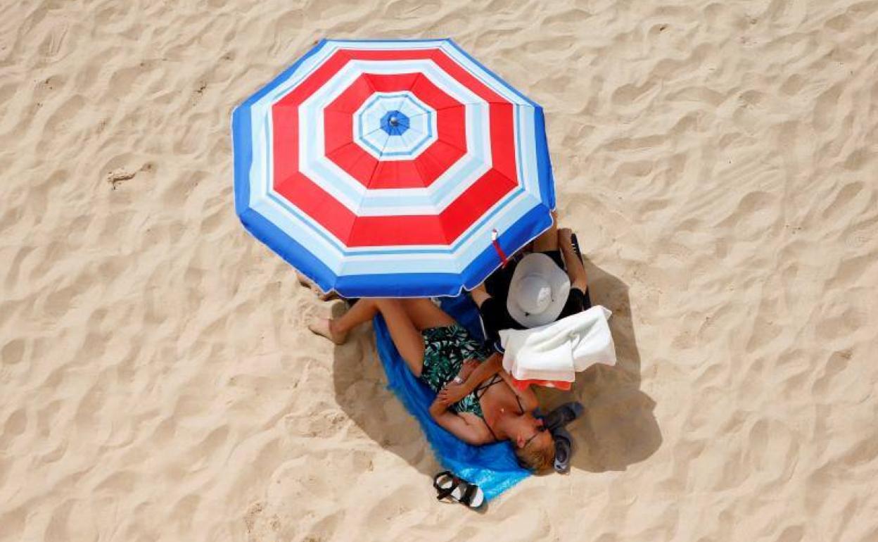 Una pareja toma el sol bajo una sombrilla.