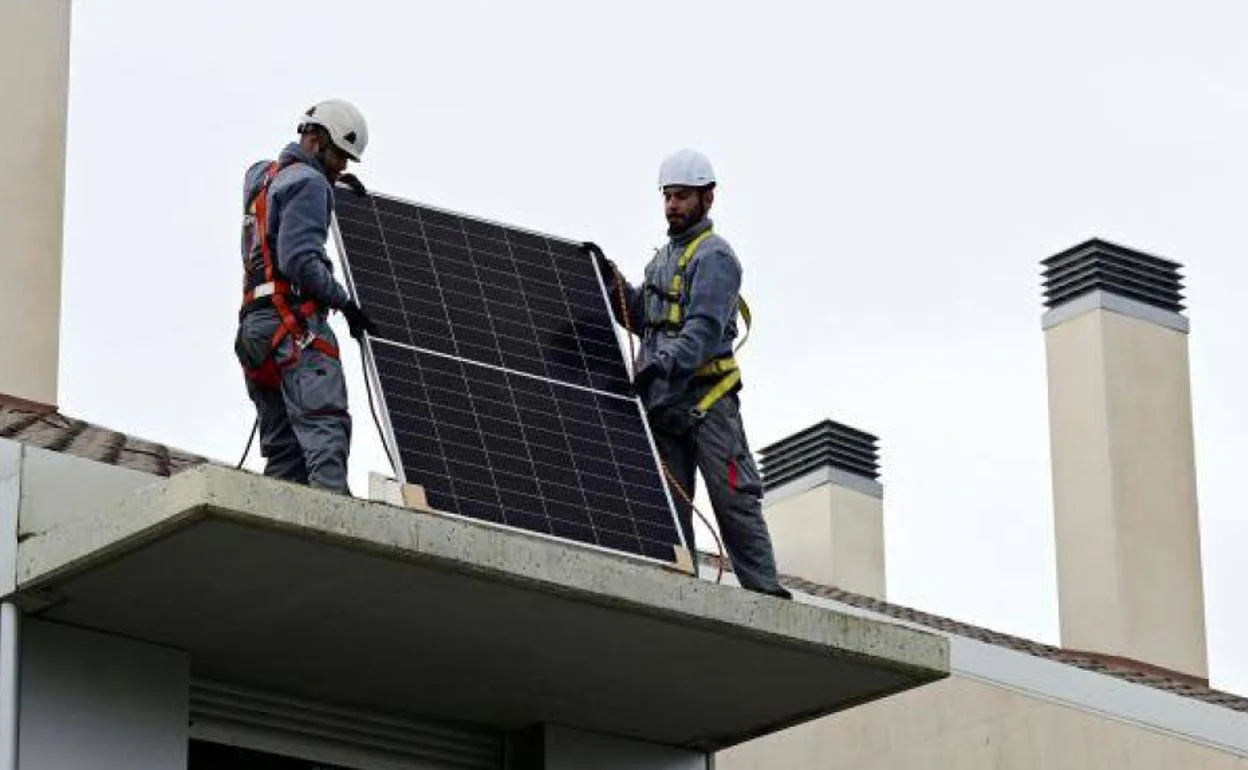 Dos operarios instalan una placa fotovoltaica en el tejado de una comunidad de viviendas.