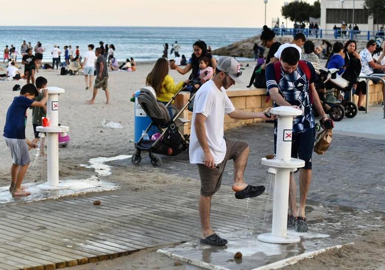 Personas se limpian los pies en la playa de El Postiguet