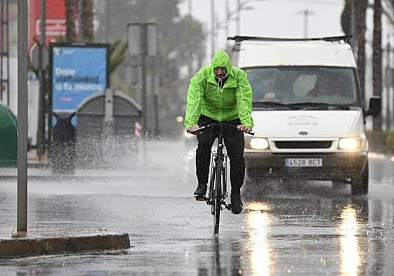 Un hombre en bicicleta se resguarda con un chubasquero bajo la lluvia
