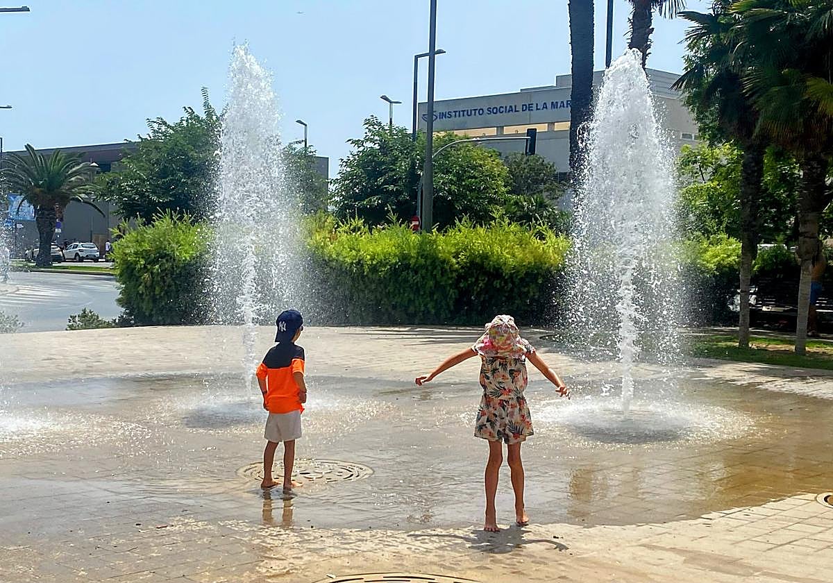 Unos niños se refrescan en una fuente.