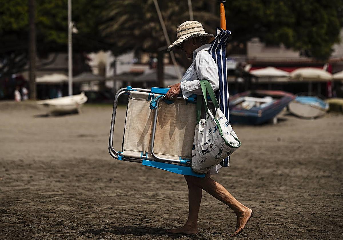 Una mujer en la playa carga con la sombrilla y la tumbona.