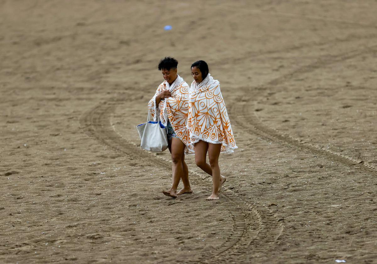 Bañistas huyen de la playa, cubiertas, tras el temporal de lluvia.