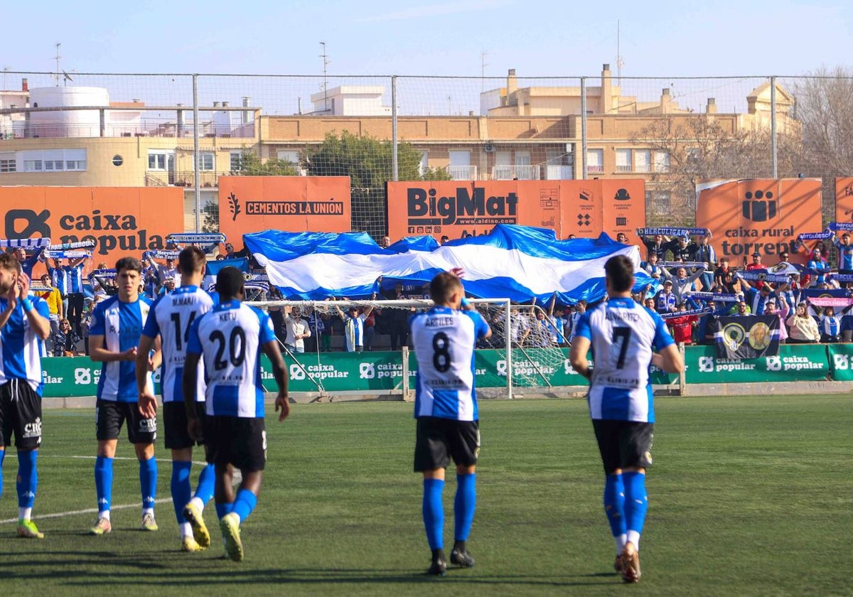 Los aficionados despliegan una bandera gigante con la salida de los jugadores al campo.